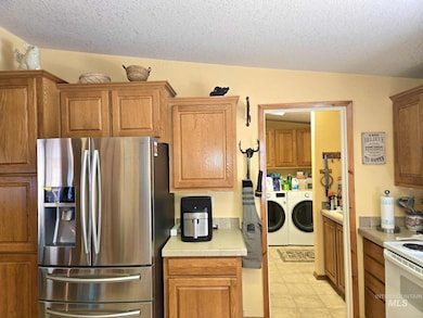 Kitchen featuring stainless steel refrigerator with ice dispenser, independent washer and dryer, white range with electric stovetop, light countertops, and brown cabinets