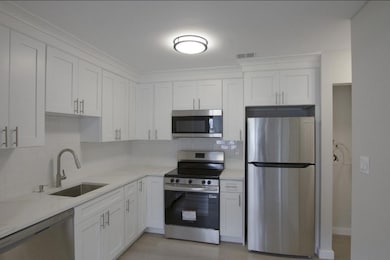 Kitchen with appliances with stainless steel finishes, white cabinetry, tasteful backsplash, and light stone counters