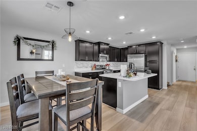 Kitchen featuring a center island with sink, decorative backsplash, appliances with stainless steel finishes, light wood-style flooring, and recessed lighting