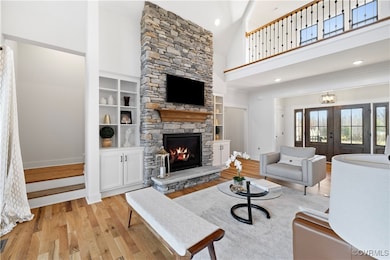 Living room with french doors, a stone fireplace, a high ceiling, and light wood-type flooring