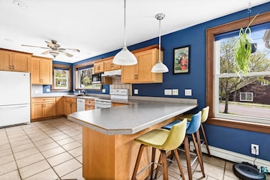 Kitchen featuring white appliances, under cabinet range hood, light tile patterned floors, a peninsula, and a kitchen bar