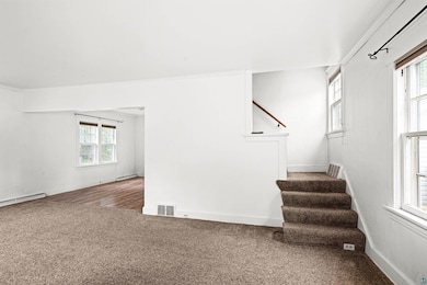 Unfurnished living room featuring stairway, healthy amount of natural light, and carpet flooring