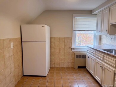 Kitchen featuring freestanding refrigerator, radiator, light tile patterned floors, tile walls, and white cabinets