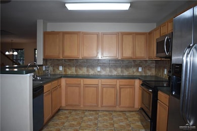 Kitchen featuring appliances with stainless steel finishes, dark countertops, decorative backsplash, and a chandelier