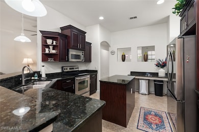 Kitchen with appliances with stainless steel finishes, dark stone countertops, decorative light fixtures, a center island, and open shelves