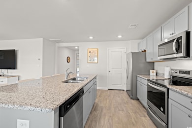 Kitchen with stainless steel appliances, light stone counters, light wood-style flooring, recessed lighting, and a center island with sink