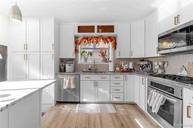 Kitchen featuring stainless steel appliances, light stone countertops, white cabinets, backsplash, and hanging light fixtures
