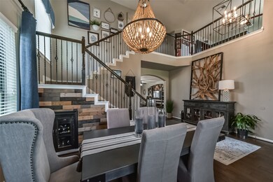 This is an elegant dining area with a modern chandelier, leading to a stylish staircase with wrought iron balusters. The space is well-lit, featuring high ceilings and a warm, neutral color palette.