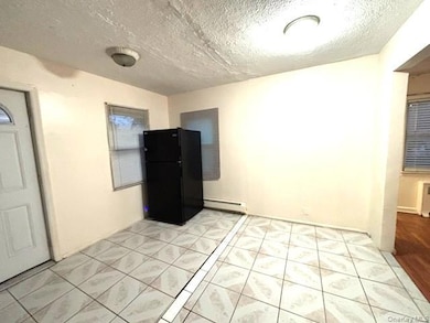 Kitchen with freestanding refrigerator, a textured ceiling, a baseboard radiator, and light tile patterned floors