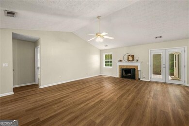 Unfurnished living room featuring ceiling fan, wood finished floors, a textured ceiling, french doors, and lofted ceiling