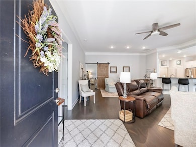 Living area with a barn door, ceiling fan, ornamental molding, wood finished floors, and recessed lighting