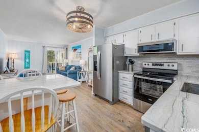 Kitchen with stainless steel appliances, backsplash, light stone countertops, light wood-style flooring, and open floor plan