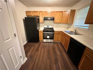 Kitchen featuring black appliances, a sink, under cabinet range hood, a textured ceiling, and light countertops