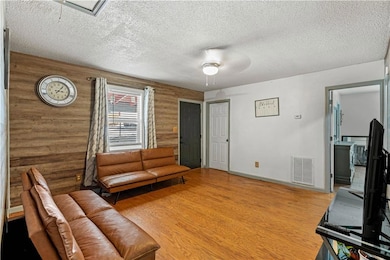 Living room featuring a ceiling fan, a textured ceiling, wood finished floors, and rustic walls