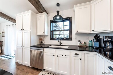 Kitchen with beamed ceiling, stainless steel dishwasher, white cabinetry, light wood-style flooring, and hanging light fixtures