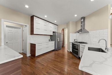 Kitchen with a sink, appliances with stainless steel finishes, modern cabinets, wall chimney range hood, and arched walkways