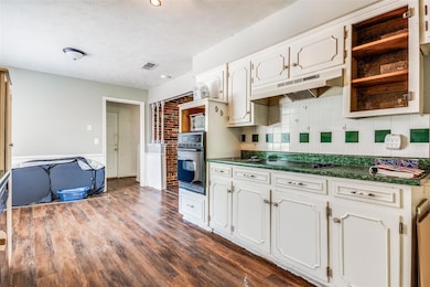 Kitchen with backsplash, brick wall, black appliances, dark hardwood / wood-style floors, and white cabinets