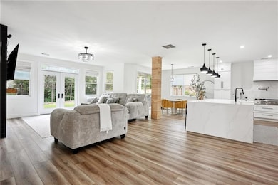 Living room with light wood-type flooring, recessed lighting, a chandelier, french doors, and decorative columns