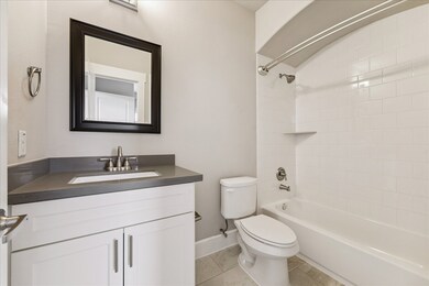 This ensuite bathroom features a sleek vanity with framed mirror, neutral tile flooring, and a tub with subway tile surround, blending style with everyday convenience.