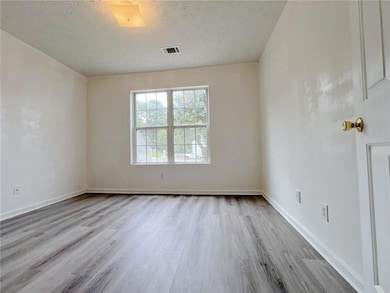 Unfurnished bedroom featuring multiple windows, wood finished floors, a textured ceiling, and baseboards