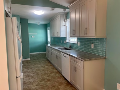 Kitchen with dark stone countertops, white appliances, backsplash, pendant lighting, and white cabinetry