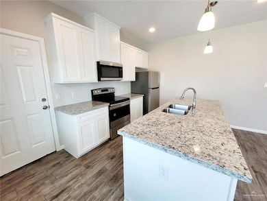 Kitchen featuring appliances with stainless steel finishes, tasteful backsplash, white cabinets, hanging light fixtures, and dark wood finished floors