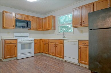 Kitchen with black appliances, a sink, ornamental molding, light wood-style flooring, and light countertops