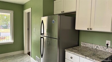 Kitchen with white cabinets, freestanding refrigerator, light stone counters, and light marble finish flooring