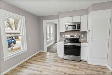 Kitchen featuring stainless steel appliances, white cabinets, tasteful backsplash, light wood-type flooring, and light stone counters