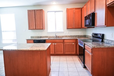 Kitchen featuring black appliances, brown cabinets, dark stone countertops, and light tile patterned flooring