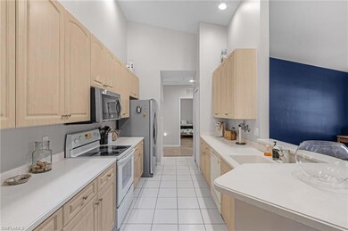 Kitchen with white appliances, light brown cabinetry, light tile patterned floors, a towering ceiling, and light countertops