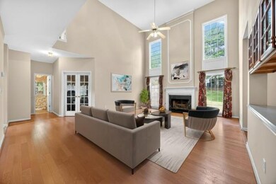 Living room with healthy amount of natural light, french doors, light wood-style floors, a towering ceiling, and a fireplace