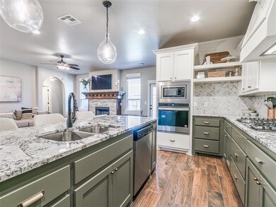 Kitchen with ceiling fan, appliances with stainless steel finishes, a fireplace, decorative light fixtures, and white cabinetry