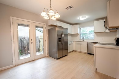 Kitchen with stainless steel appliances, light countertops, pendant lighting, backsplash, and white cabinetry