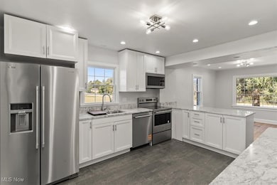 Kitchen featuring stainless steel appliances, a peninsula, white cabinets, light stone countertops, and recessed lighting