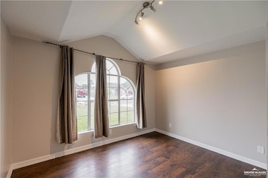 Spare room featuring lofted ceiling, dark wood-style floors, baseboards, and track lighting