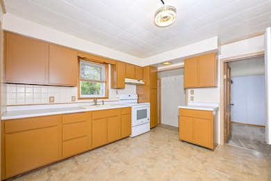 Kitchen with white electric range oven, a sink, light countertops, under cabinet range hood, and decorative backsplash