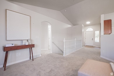 Interior space with carpet flooring, vaulted ceiling, an upstairs landing, and arched walkways