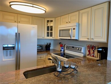 Kitchen featuring white appliances, glass insert cabinets, white cabinets, and dark stone countertops