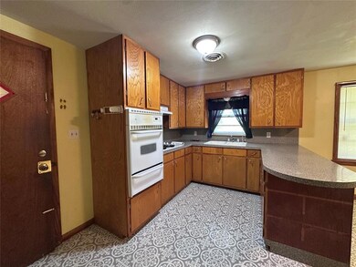 Kitchen with a warming drawer, white appliances, a peninsula, brown cabinetry, and under cabinet range hood