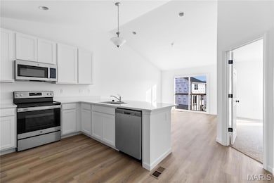 Kitchen featuring appliances with stainless steel finishes, white cabinets, a peninsula, lofted ceiling, and light wood-style floors