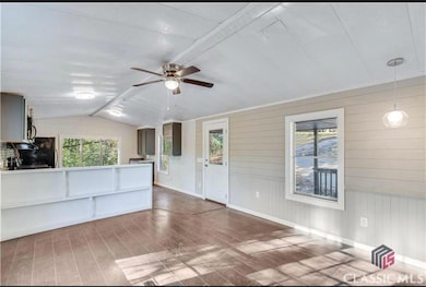 Unfurnished living room with wood finished floors, lofted ceiling, healthy amount of natural light, a ceiling fan, and wooden walls