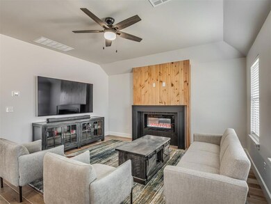 Living area featuring vaulted ceiling, wood finished floors, a glass covered fireplace, and ceiling fan