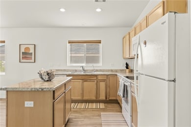 Kitchen with white appliances, plenty of natural light, a center island, recessed lighting, and light wood-style floors