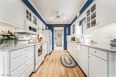 Kitchen with decorative backsplash, white cabinets, light wood-type flooring, and white appliances