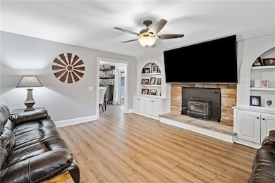 Living area featuring a ceiling fan, built in features, baseboards, light wood-style floors, and a fireplace