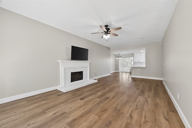 The expansive living area offers an open concept design, featuring modern wood-look flooring, a cozy fireplace with a mounted TV, and a clear view to the kitchen.