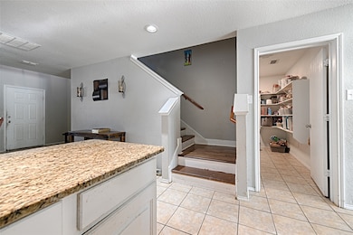 Kitchen with light tile patterned flooring, a textured ceiling, light stone counters, and white cabinetry