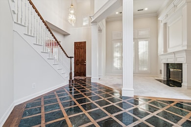 Foyer entrance featuring healthy amount of natural light, a towering ceiling, inlaid floor details, ornamental molding, and a high end fireplace