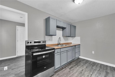 Kitchen featuring stainless steel electric stove, gray cabinetry, tasteful backsplash, a textured ceiling, and light wood finished floors